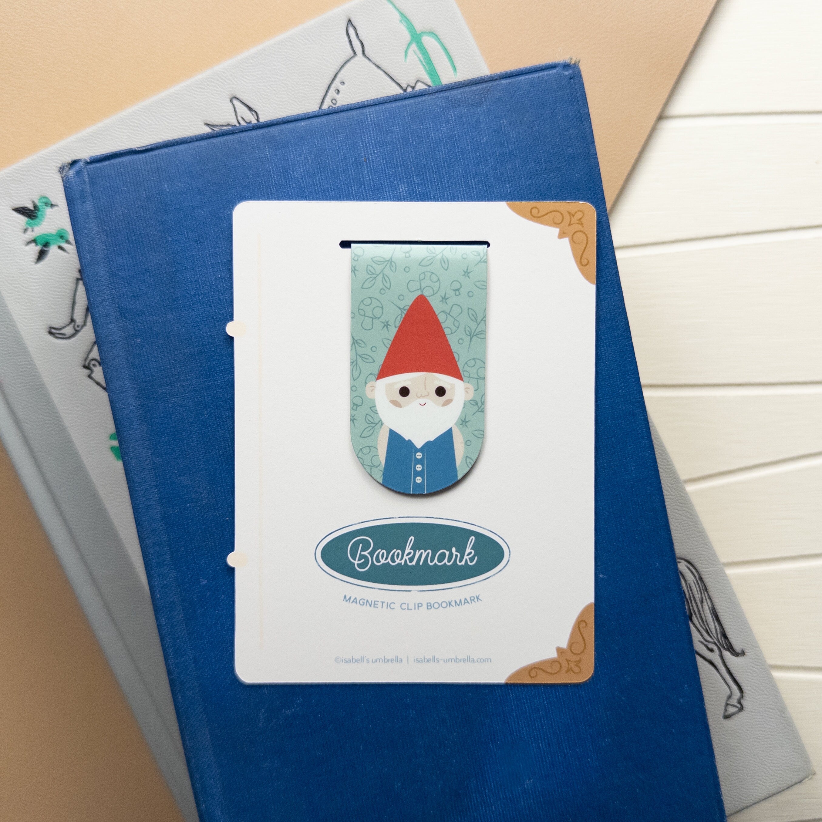 Magnetic bookmark featuring an illustrated gnome packaged and sitting on top of a stack of books.