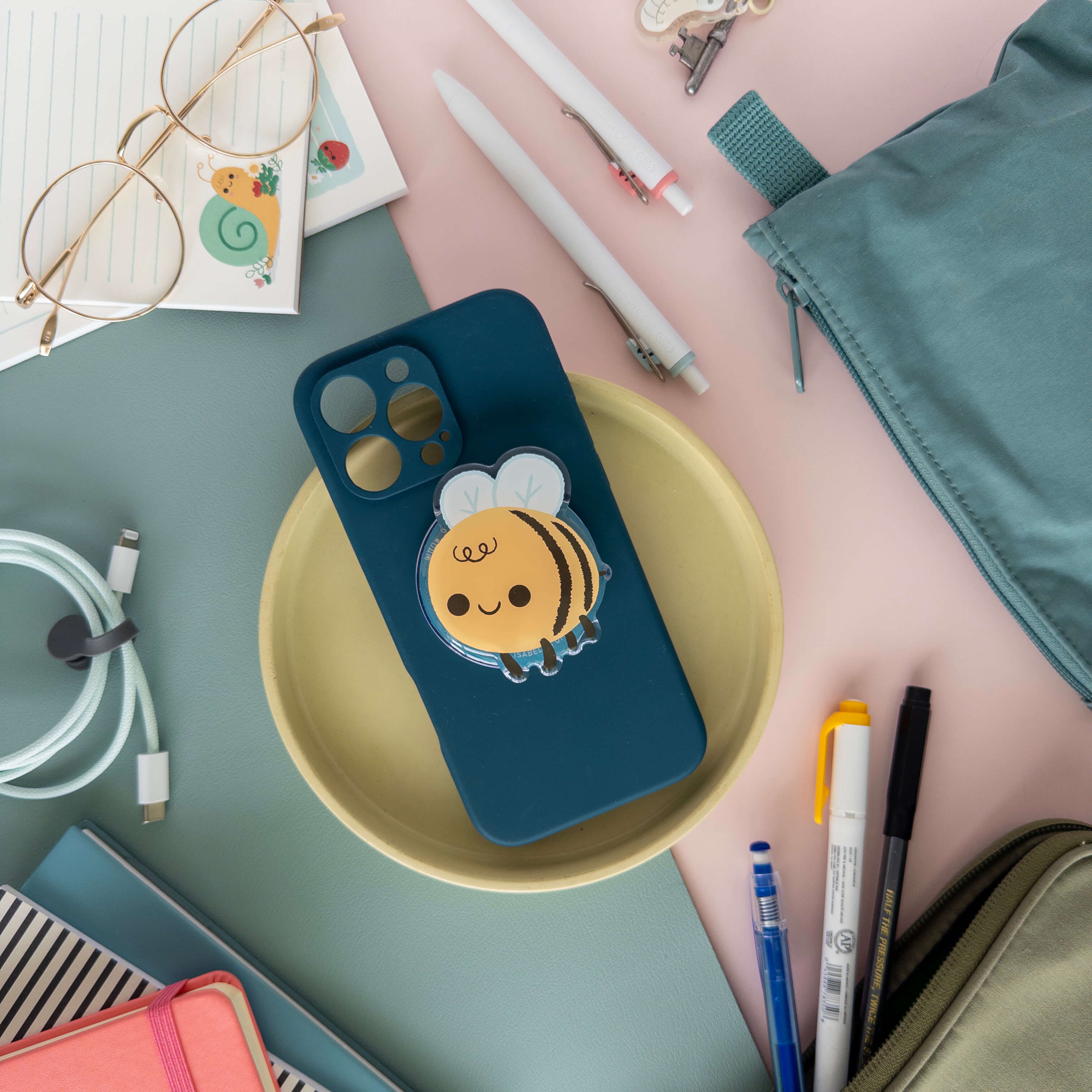 Phone case with a bee magnetic phone grip on a desk with stationery items