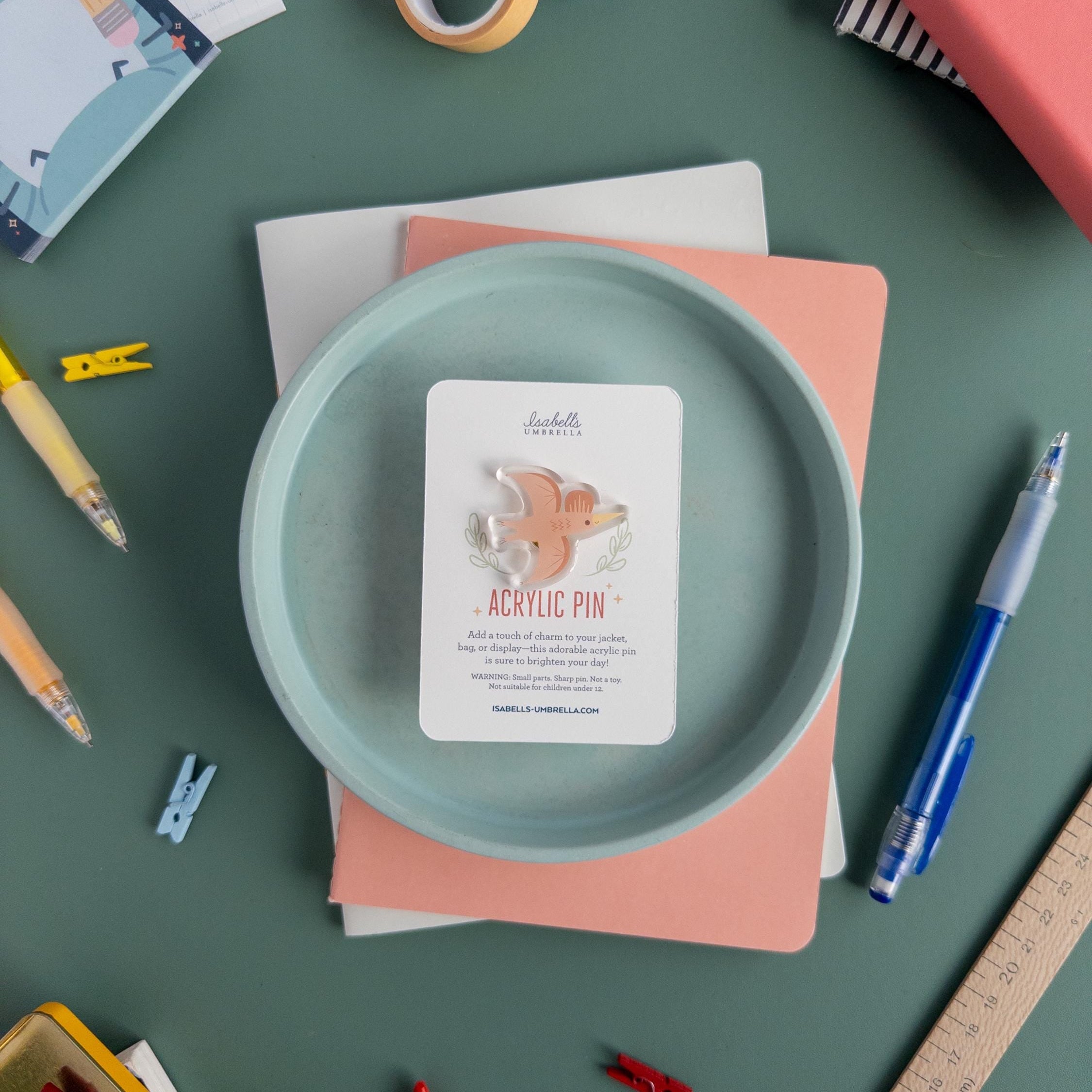 A single cute pterodactyl acrylic pin with glossy epoxy finish, kawaii dinosaur enamel-style accessory for jackets, backpacks, and pin boards