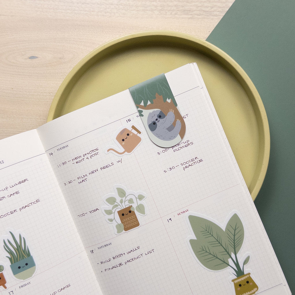 Detail shot of an illustrated magnetic clip bookmark featuring a sloth in a tree on a calendar page of a planner.