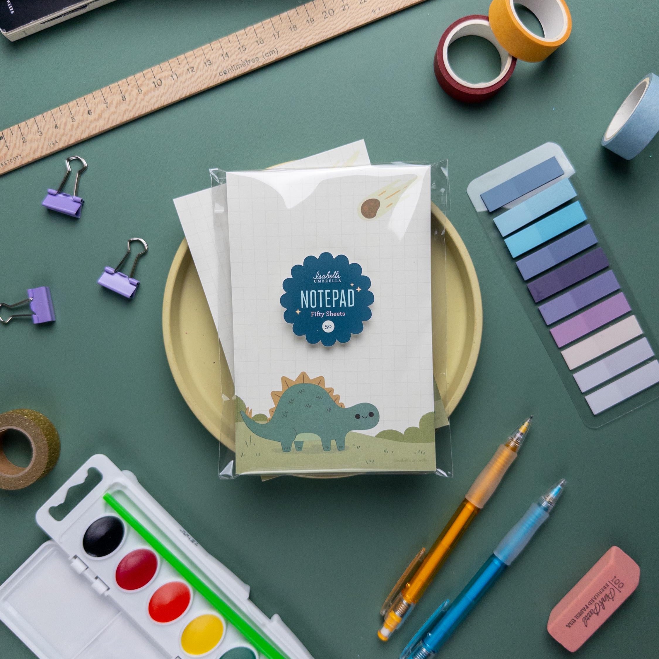 Cute kawaii stegosaurus dinosaur notepad with grid paper, 50 tear-off sheets, and sturdy chipboard backing, perfect for kids and stationery lovers.