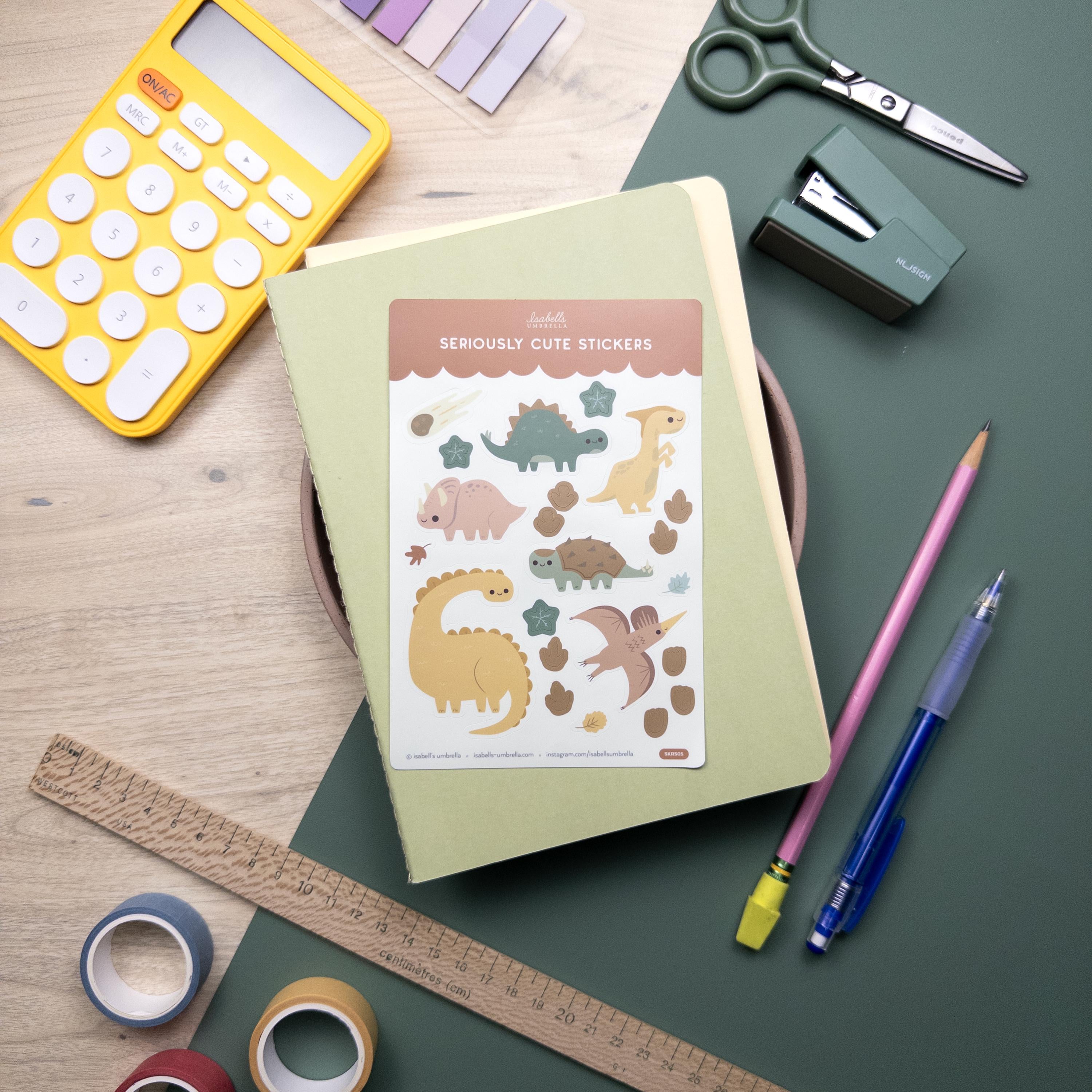 Dinosaur themed sticker sheet set atop a green notebook.