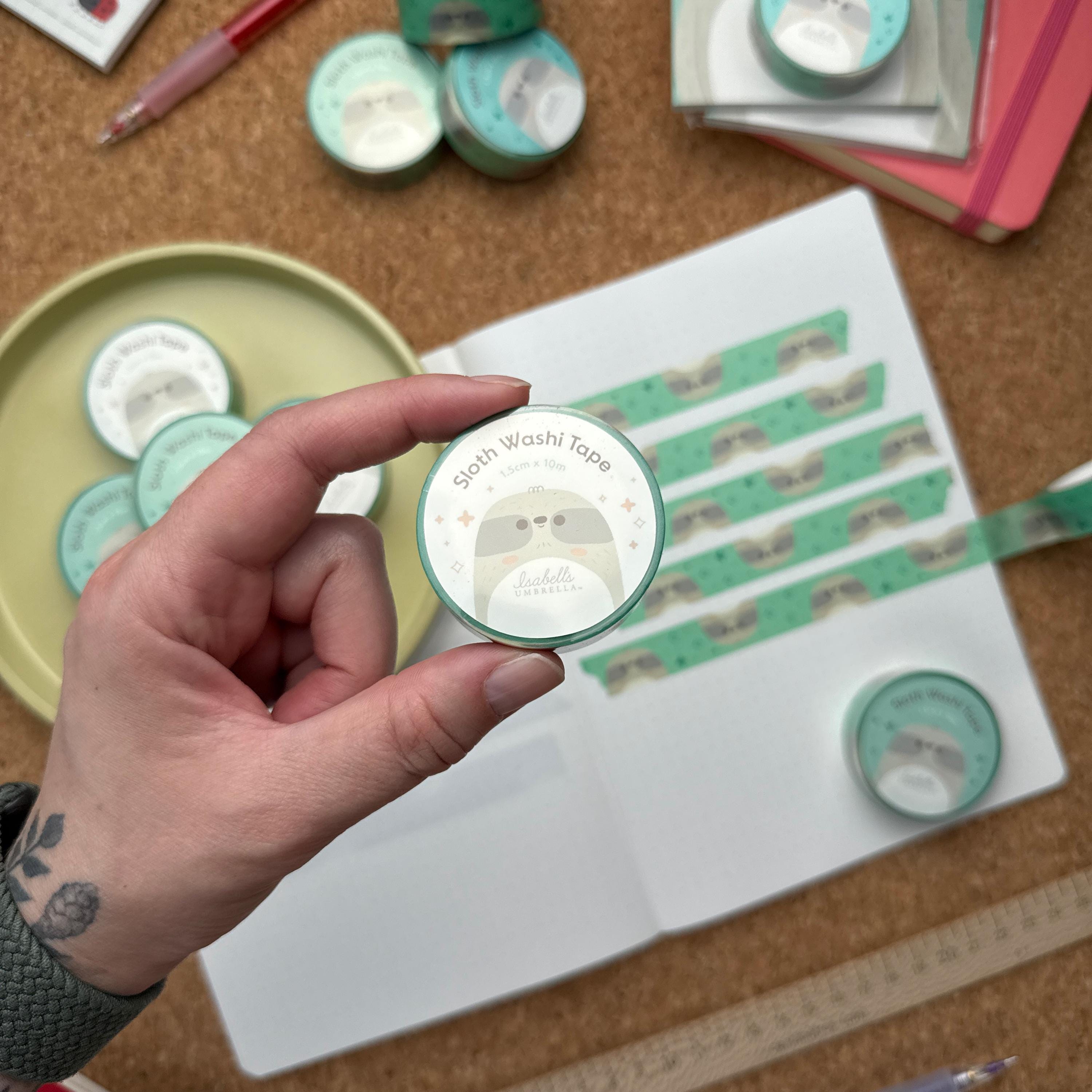 Hand holding a roll of cute smiling sloth washi tape, kawaii decorative tape for planners, journals, and scrapbooks, easy to tear and residue-free.