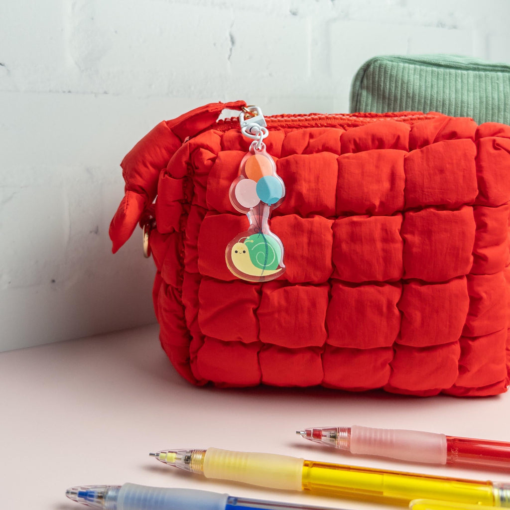 Snail carried by balloon acrylic keychain attached to the zipper of a textured red tote bag