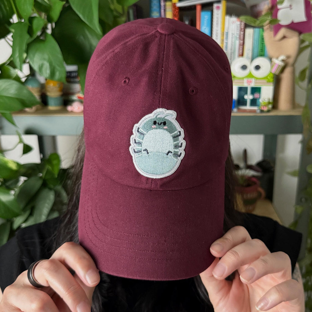 Woman wearing a maroon cotton twill dad hat with embroidered roly poly patch, adjustable baseball cap with low-profile fit for cute minimalist style.