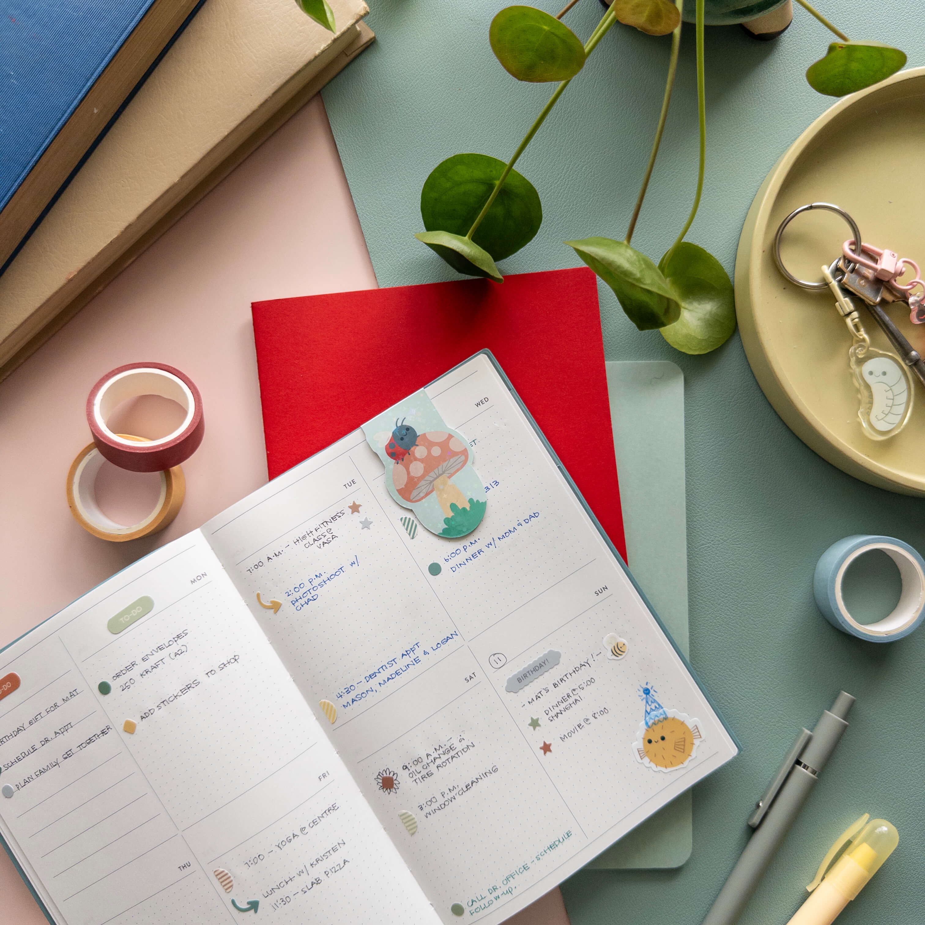 Open notebook with a bookmark of a  mushroom with ladybug on a desk with stationery items