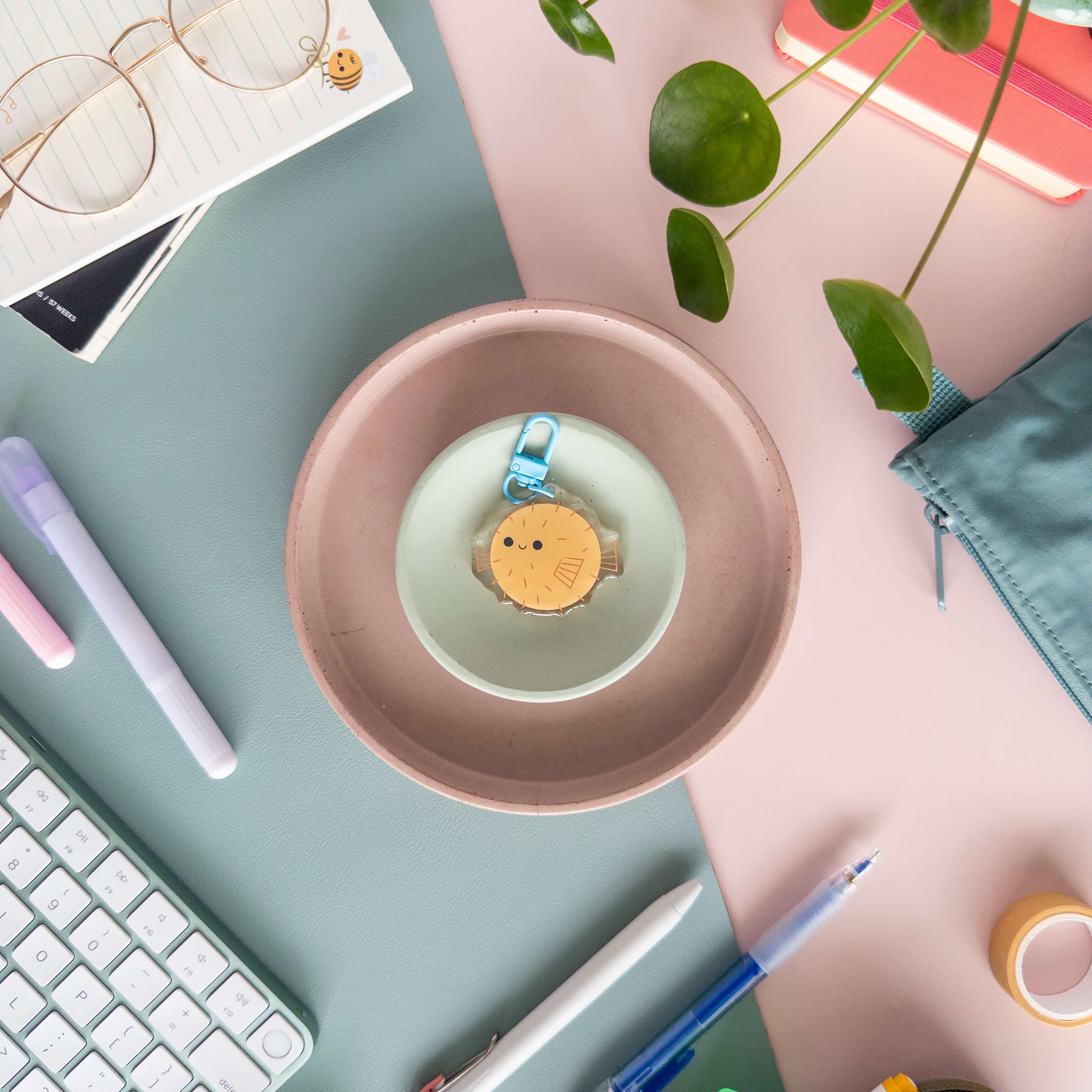 Desk setup with a pink bowl containing a small acrylic keychain of a yellow pufferfish .
