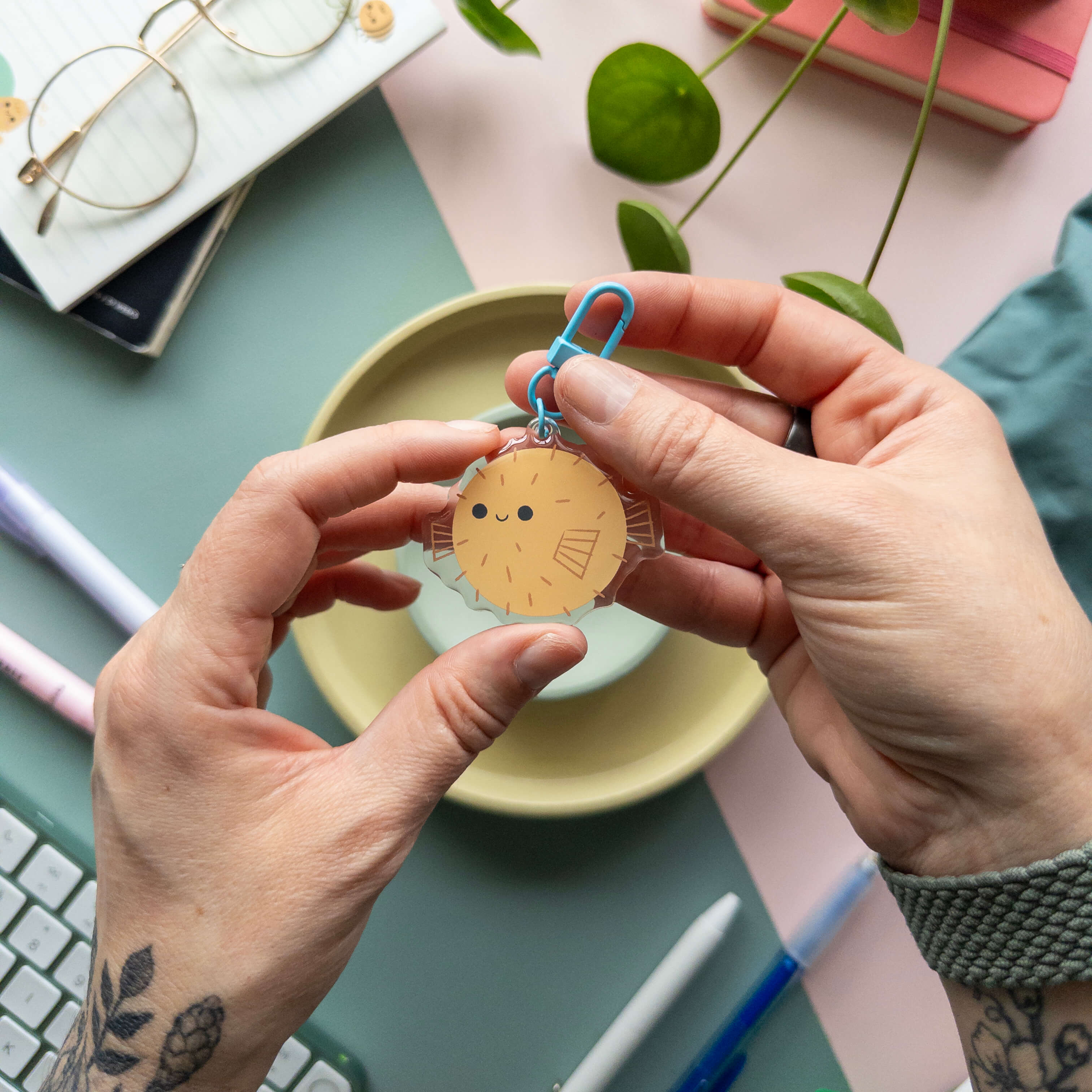Person holding an acrylic pufferfish keychain over a desk with stationery items.