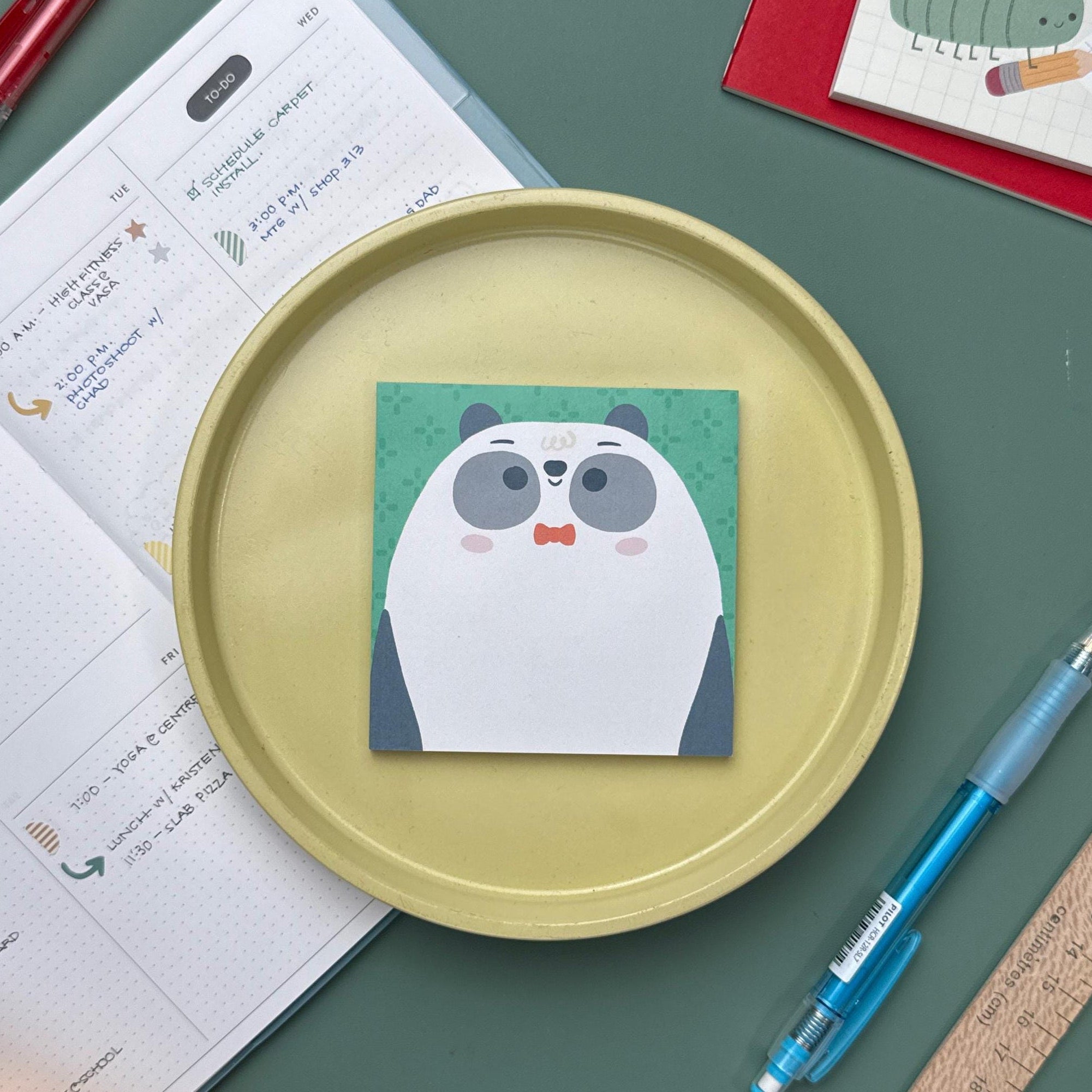 A cute panda bear bowtie sticky notepad with green background, surrounded by kawaii stationery, journal, and pens on a desk.