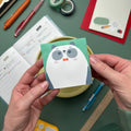 Person holding a cute panda bear bowtie sticky notepad with green background, surrounded by kawaii stationery, journal, and pens on a desk.