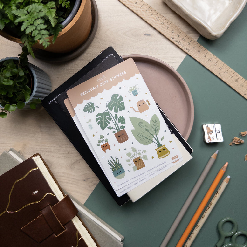 Sticker sheet of illustrated houseplants pictured on top of a stack of notebooks and surrounded by other office type materials.