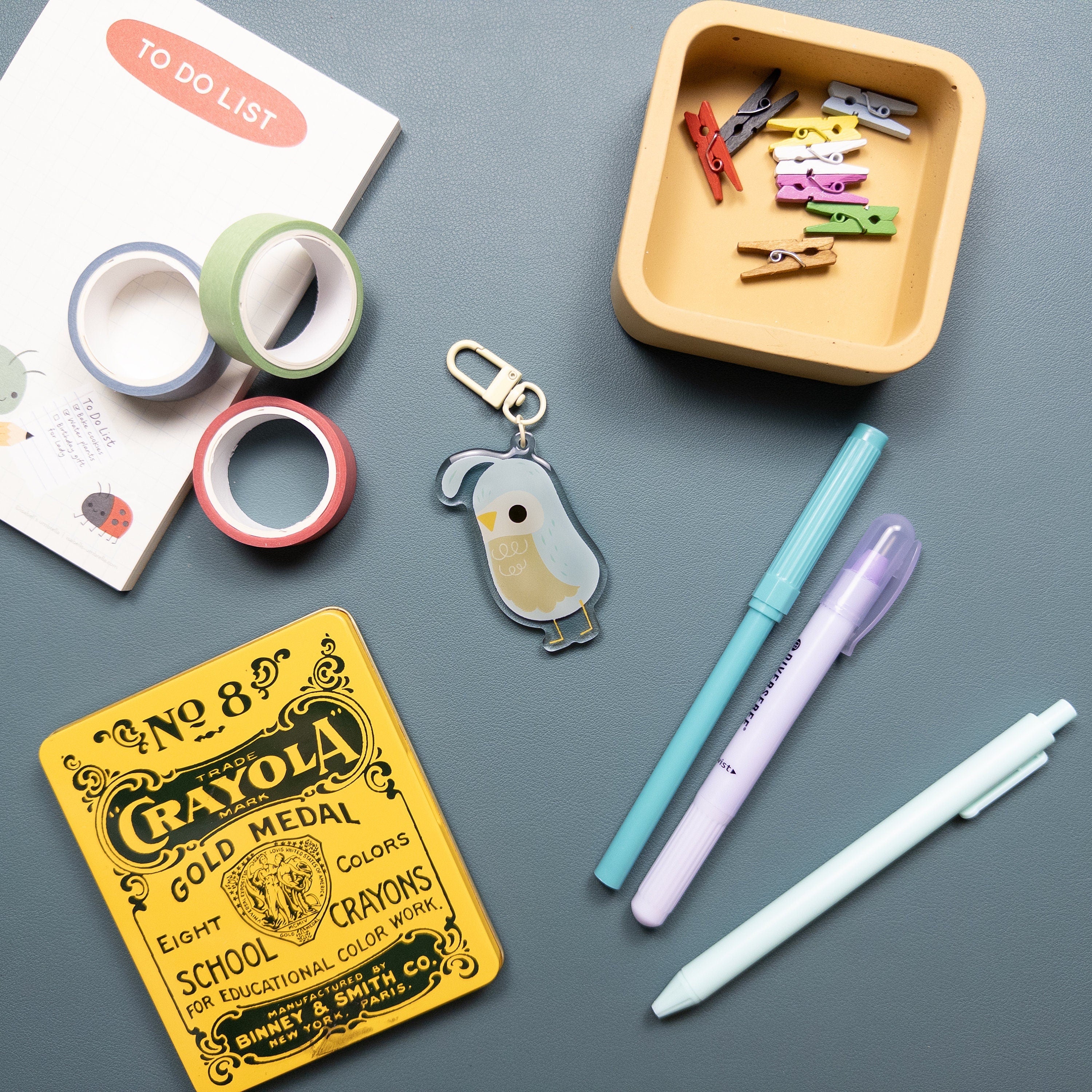 Acrylic keychain featuring an illustration of a quail sitting with an array of office supplies around it.