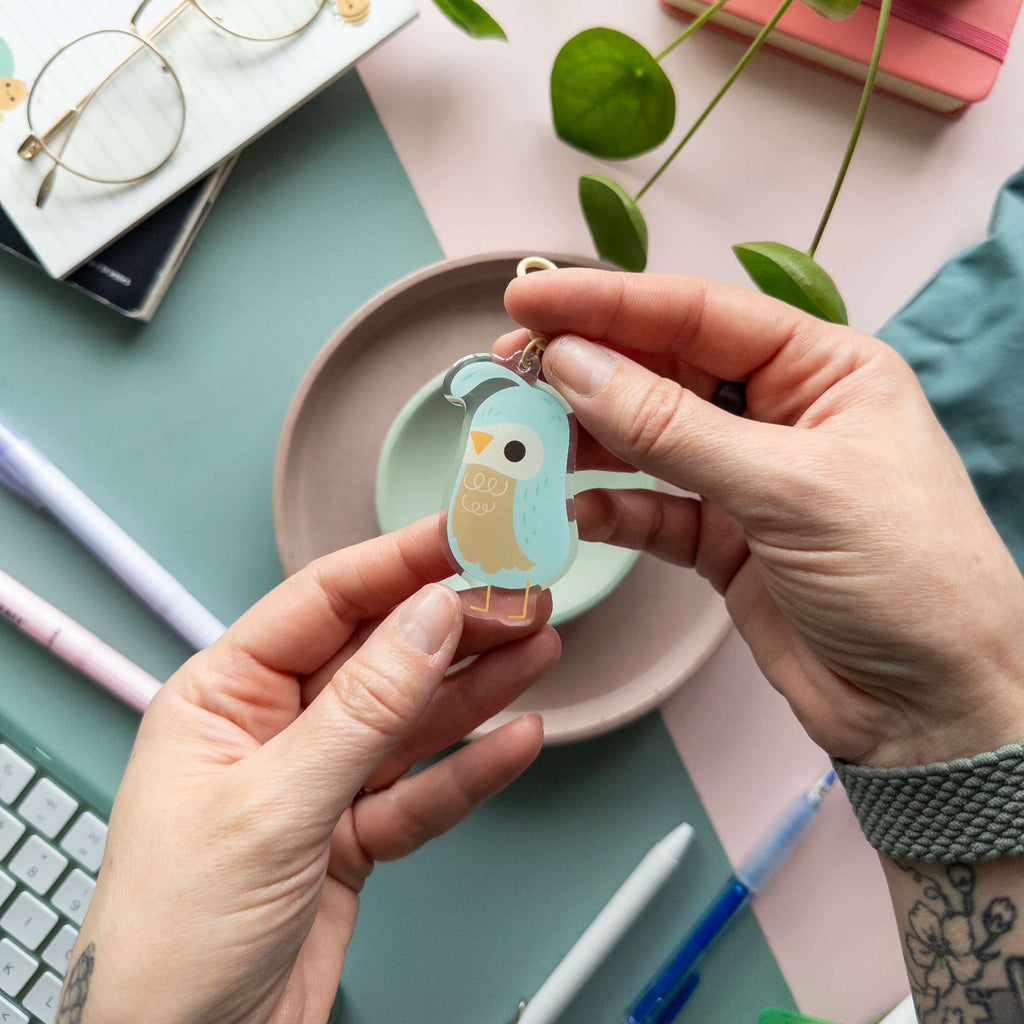 Person holding a quail-shaped keychain on a desk with stationery items.