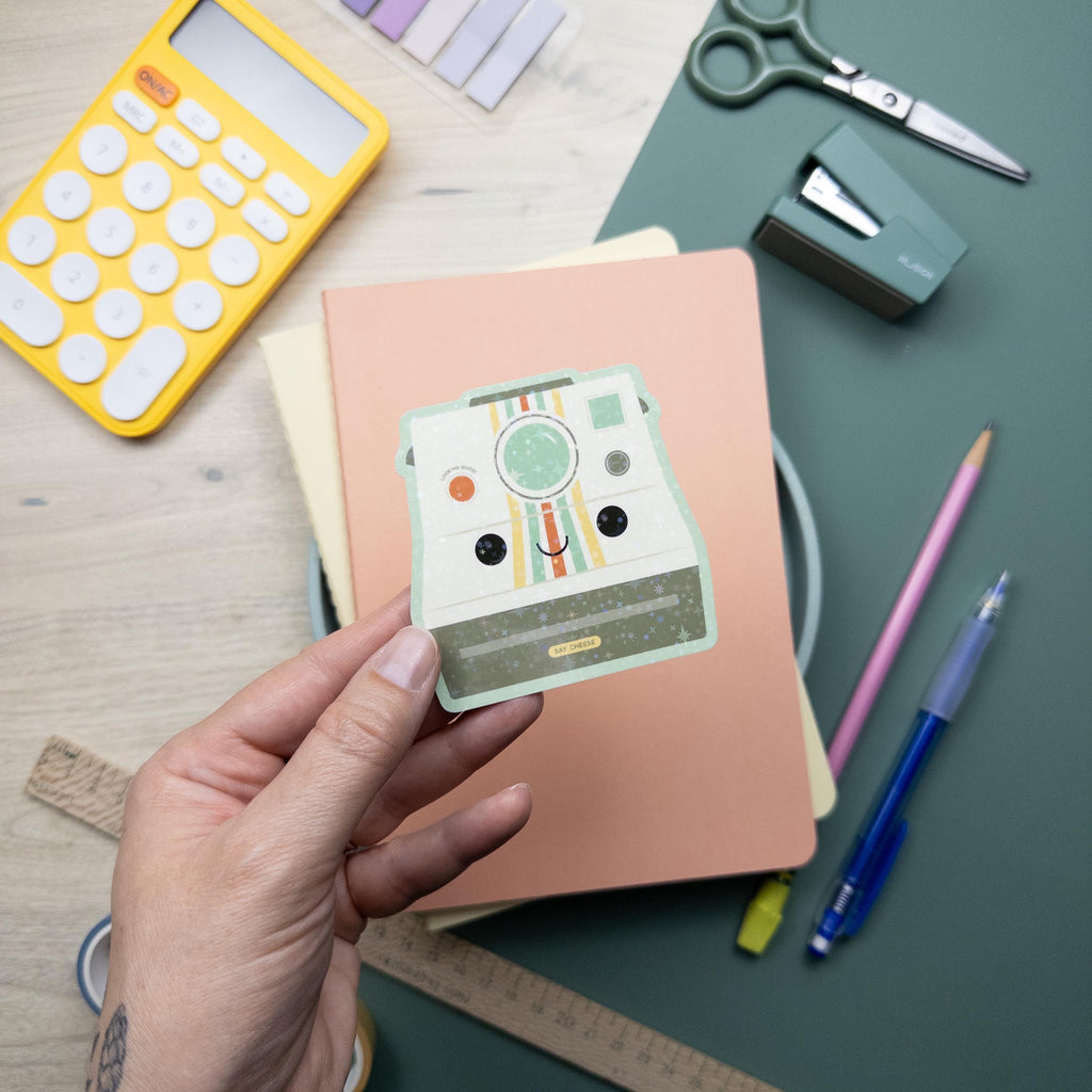 Hand holding a cute vintage camera glitter vinyl sticker, waterproof and durable photography decal for laptops, water bottles, and journals.