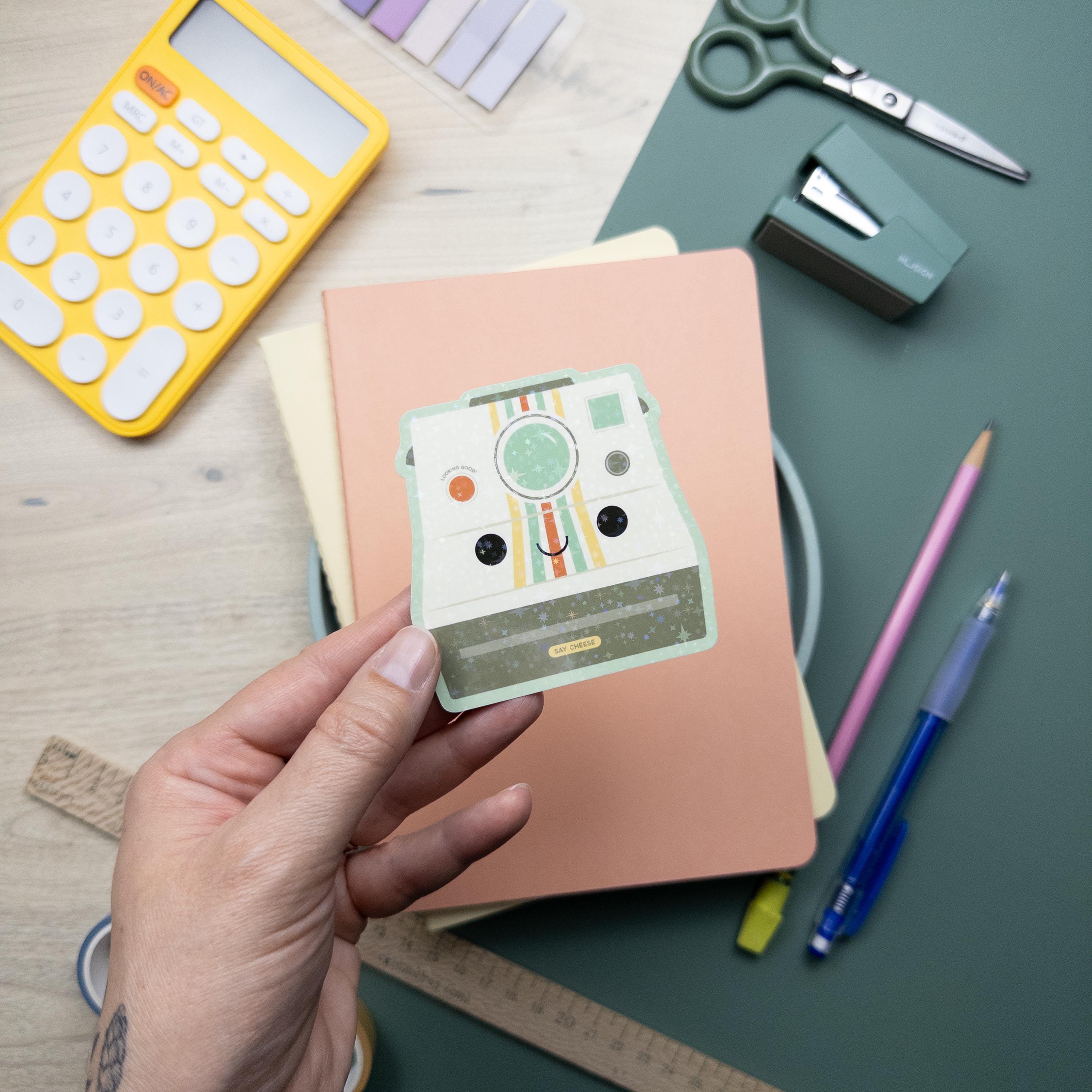 Hand holding a cute vintage camera glitter vinyl sticker, waterproof and durable photography decal for laptops, water bottles, and journals.