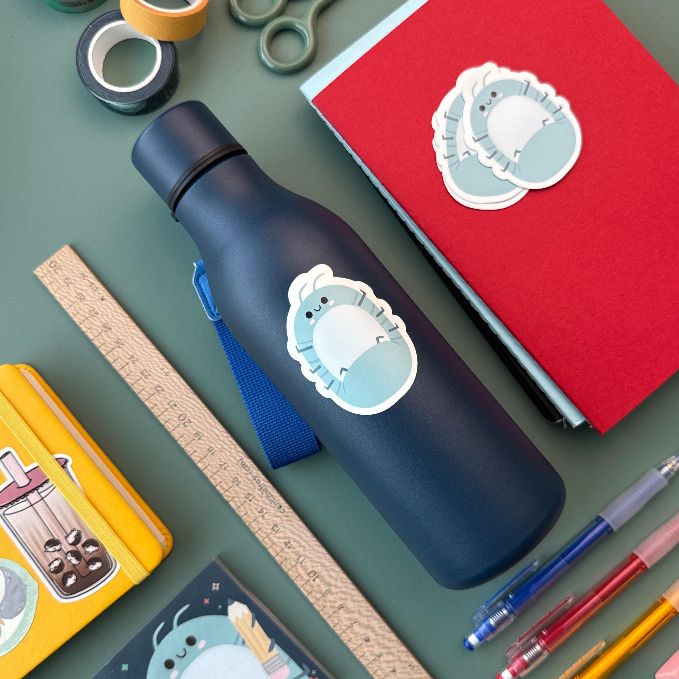 Cute roly poly isopod sticker on a navy blue water bottle, surrounded by colorful pens, washi tape, and a ruler. This waterproof vinyl sticker is perfect for decorating bottles, laptops, and school supplies.