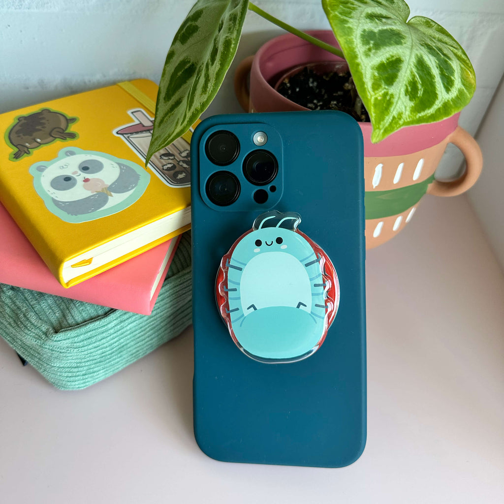 Blue phone case with a magnetic phone grip of a roly poly on a white surface with books and a plant.