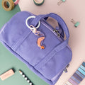 Purple pencil case with a Shrimp acrylic charm keychain attached on a colorful background with stationery items