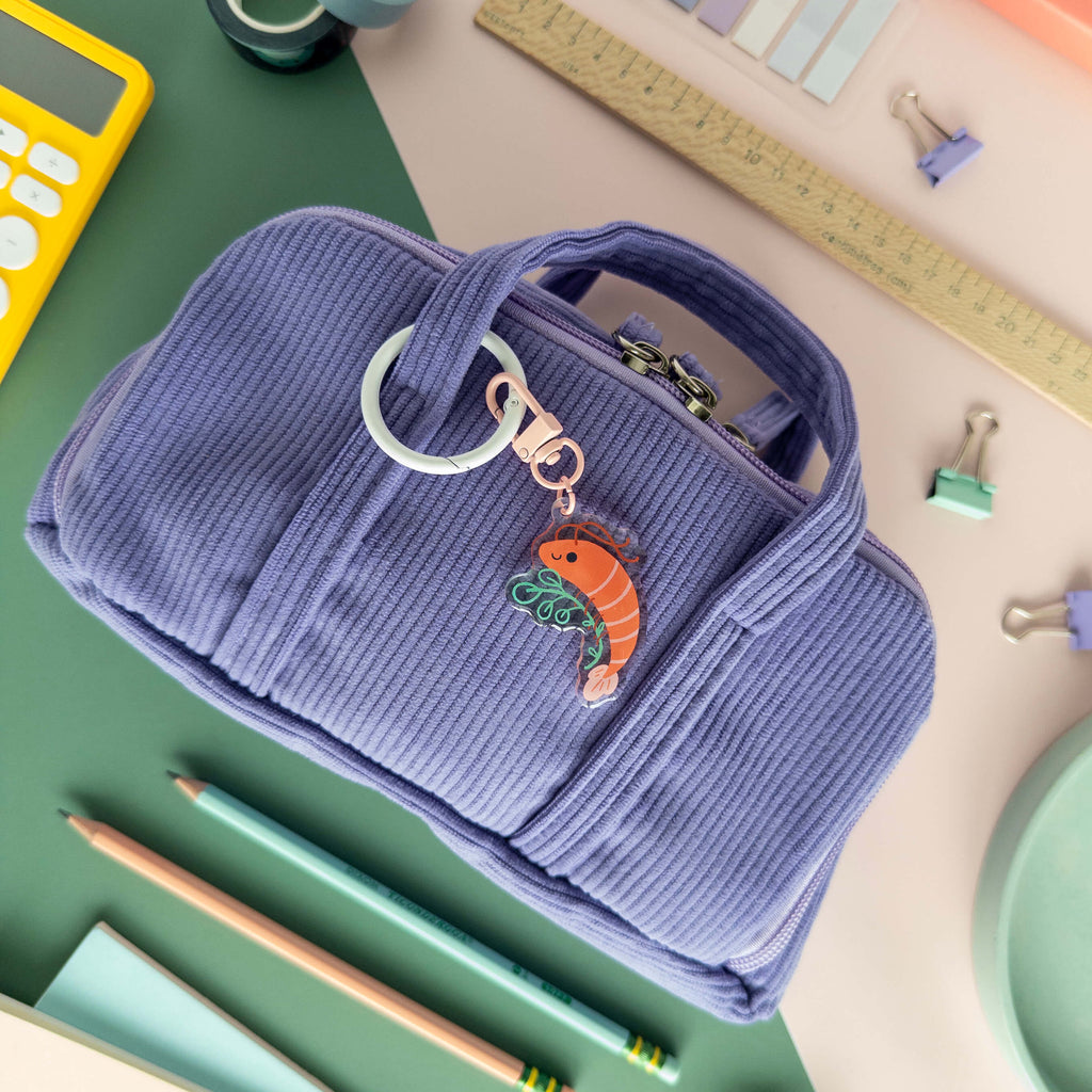 Blue pencil case with a acrylic shrimp charm on a desk with stationery items