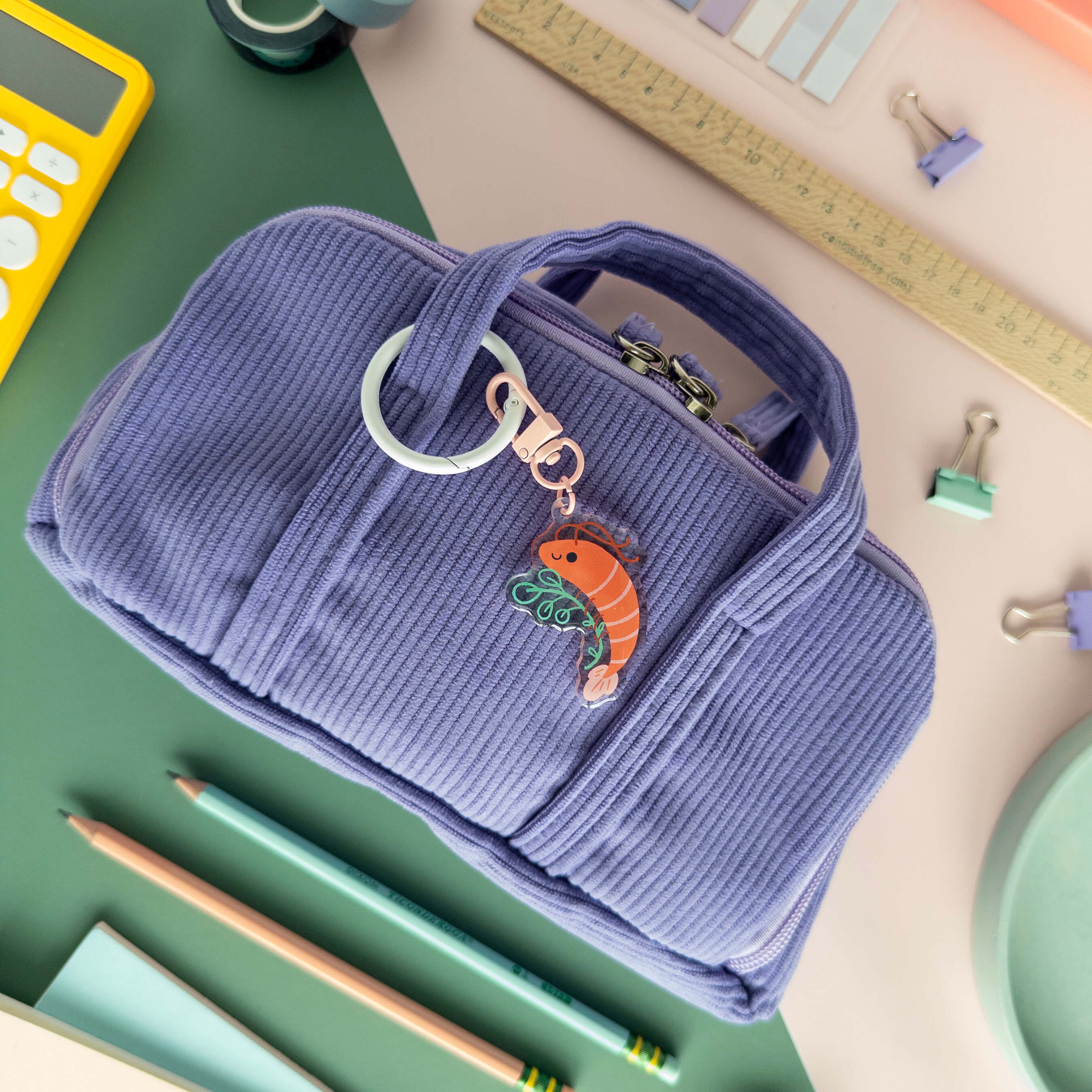 Blue pencil case with a acrylic shrimp charm on a desk with stationery items