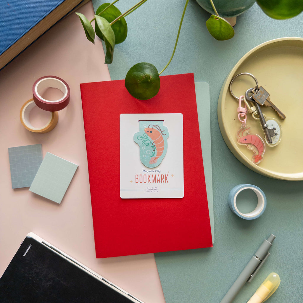Red notebook with a magnetic shrimp bookmark on a colorful surface with stationery items.