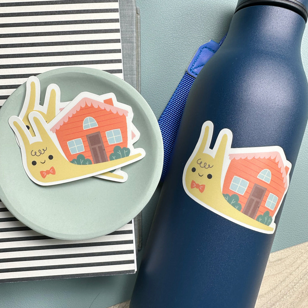 Stack of illustrated snail stickers in a small bowl sitting beside a water bottle with the same snail sticker on it.