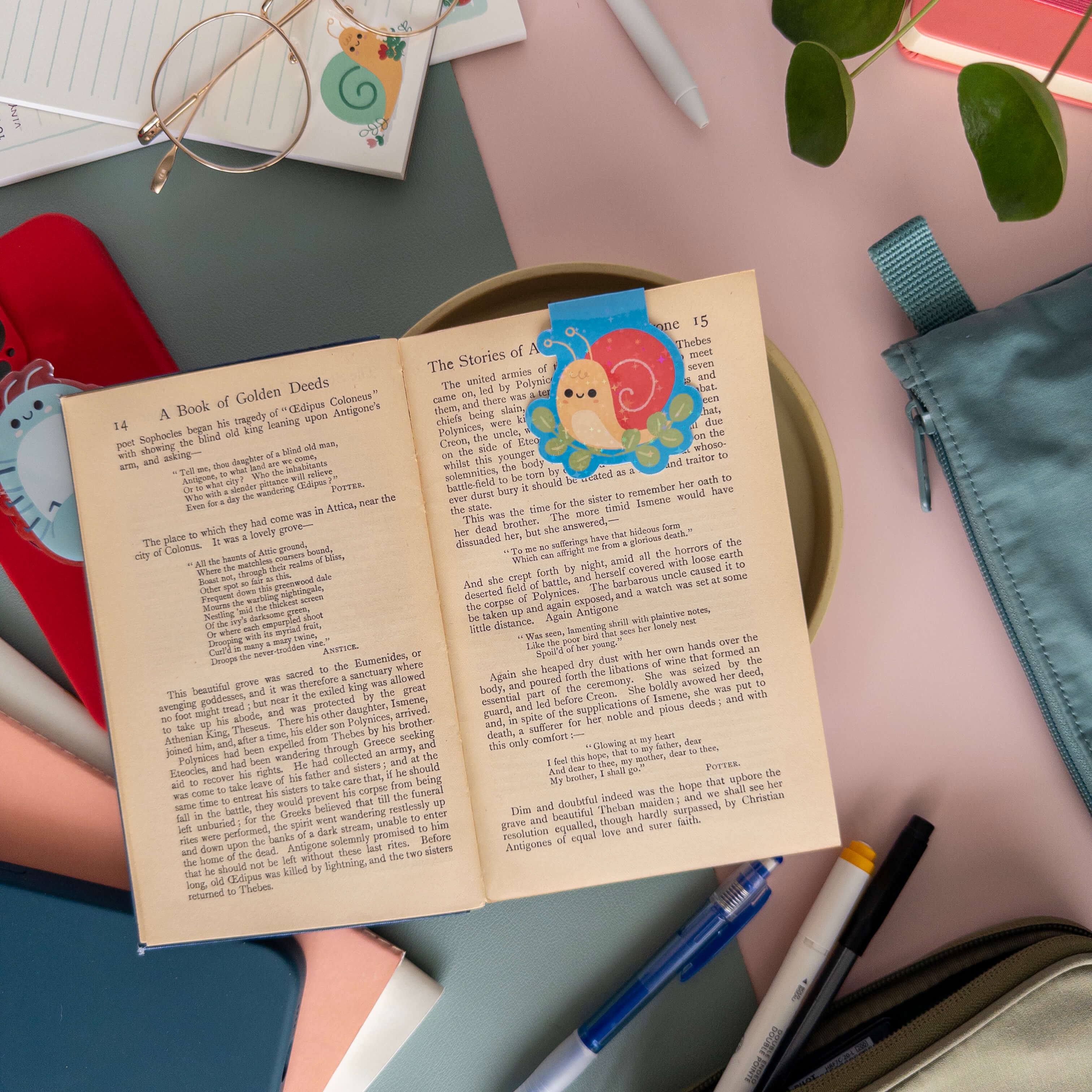 Open book with a magnetic yellow snail bookmark on a desk with stationery items