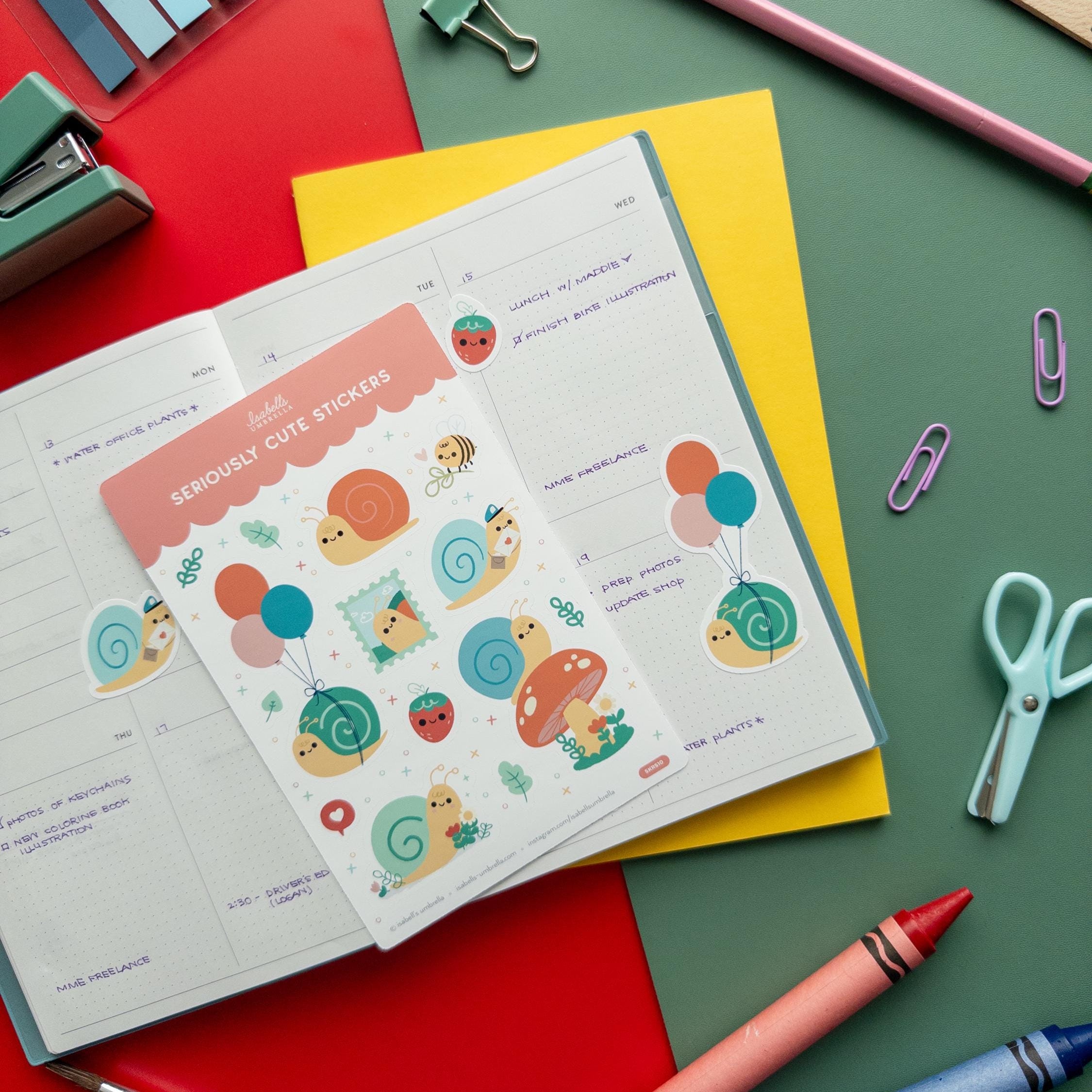 Kawaii snail sticker sheet next to an open planner with stickers applied, surrounded by school and art supplies on a red and green background.