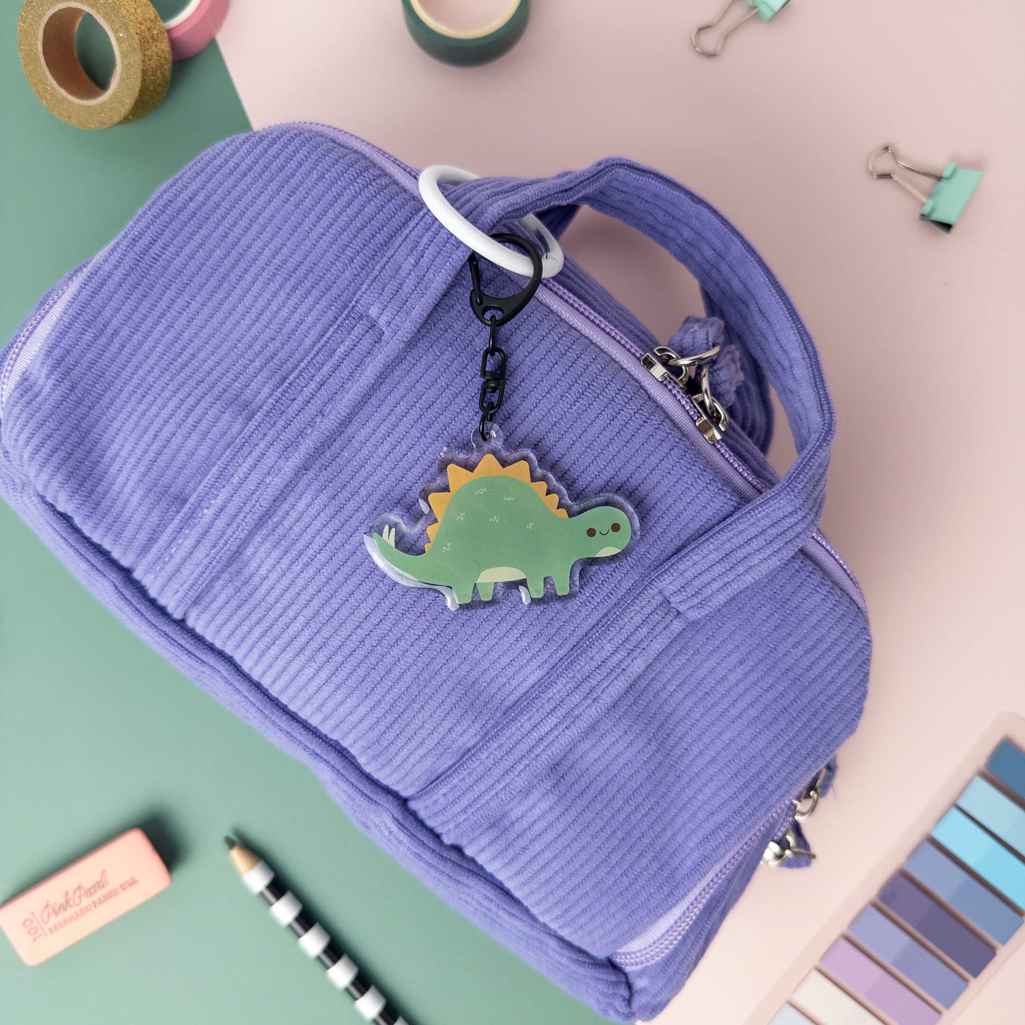 Purple bag with a dinosaur charm on a colorful background which links to the shop all collection