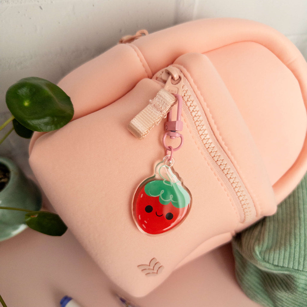 Small pink backpack with a strawberry-shaped keychain on a light background