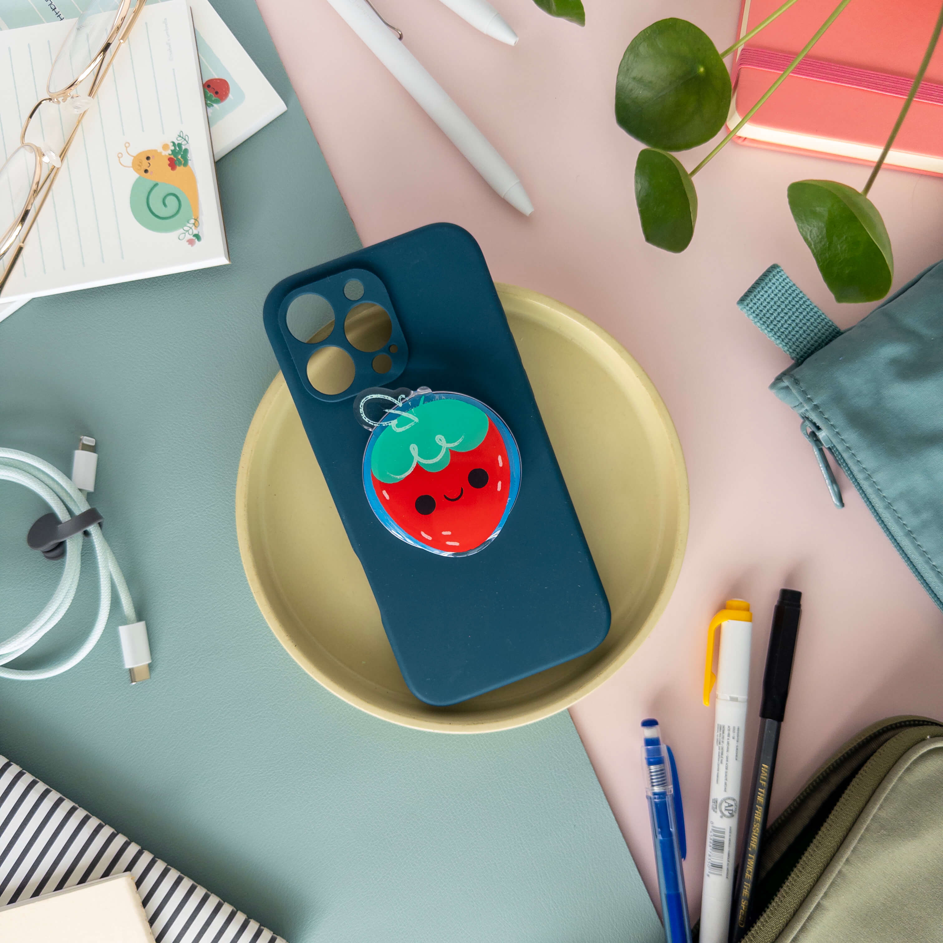 Phone case with a strawberry designed magnetic phone grip on a desk with stationery items