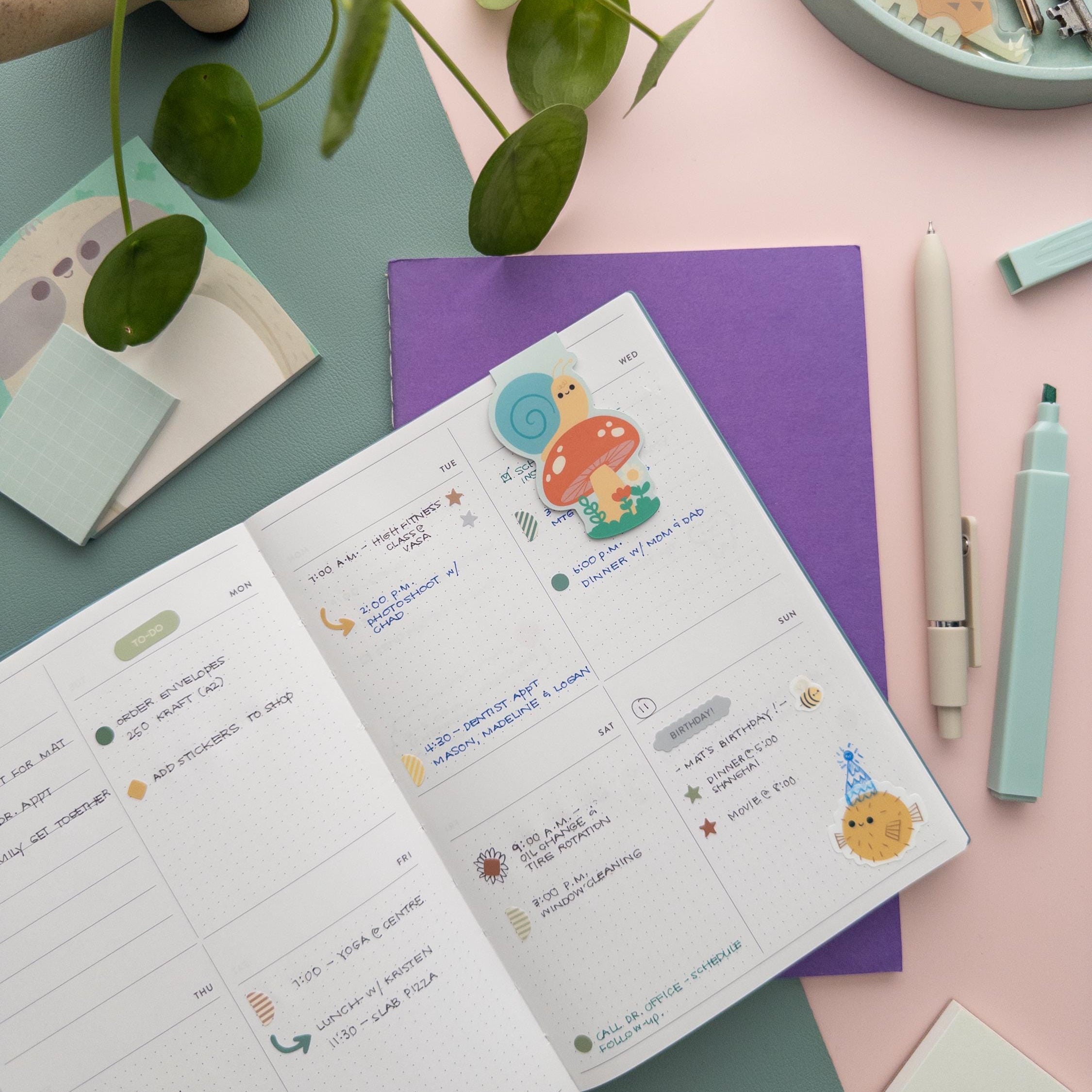 Snail and mushroom magnetic bookmark clipped on an open planner page, cozy cottagecore reading accessory for book lovers.